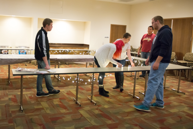 Five students work together to string white Christmas lights around the main dining table as they set up for the event. 