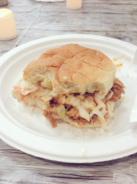 On the left, there is a close-up shot of a partially eaten pulled pork sandwich with coleslaw in it. The sandwich is on a white paper plate sitting on top of a faux wood table cloth. On the right, there is a photo that includes a shot of the main course on the table from a distance. Mason jars of iced tea, lanterns, candles, salt and pepper shakers, and silverware are also visible on the table. Two student participants are seen on their smartphones tweeting about their experiences. 